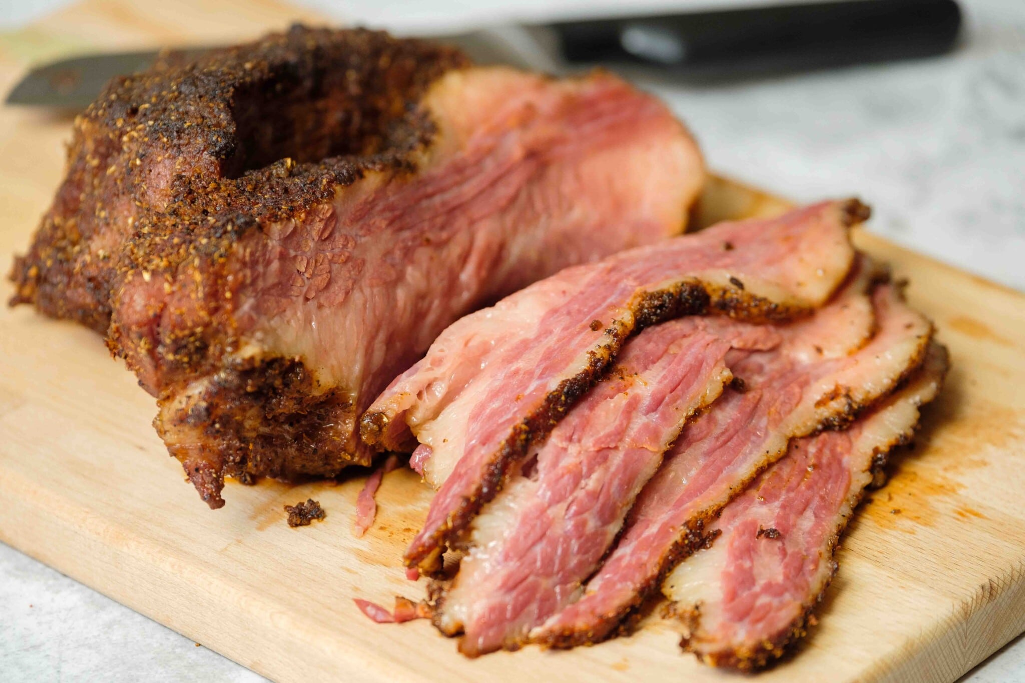 Close up horizontal shot - sliced pieces of brisket on a wooden cutting board with a chef's knife laying next to the board