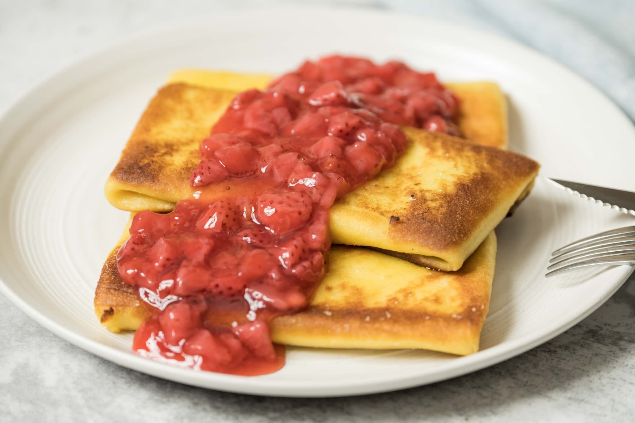 Cheese blintzes topped with a luscious strawberry sauce on a white plate