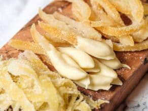 Horizontal shot - close up of candied lemon peels on a wooden cutting board on marble counter. Large peels, small peels, peels dipped in white chocolate.