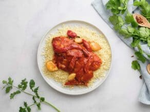 Horizontal overhead shot of fish in tomato sauce on a bed of couscous on a white plate.