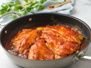 Horizontal shot of a sautee pan filled with white fish fillets in tomato sauce.