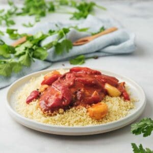 Horizontal shot of fish in tomato sauce on a bed of couscous on a white plate.