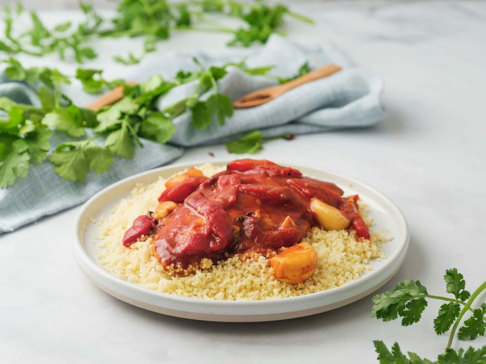 Horizontal shot of fish in tomato sauce on a bed of couscous on a white plate.