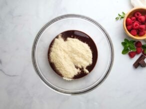 Overhead horizontal shot of a glass mixing bowl containing melted chocolate and almond flour.