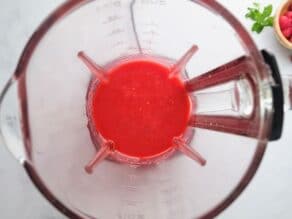 Overhead horizontal shot of a blender filled with fresh raspberry puree.