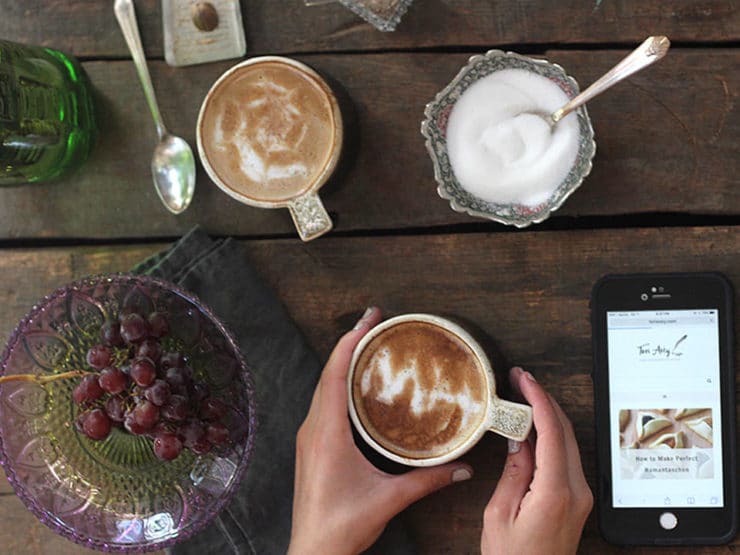 Two cups of coffee with latte art and a bowl of sugar on top of a wooden table