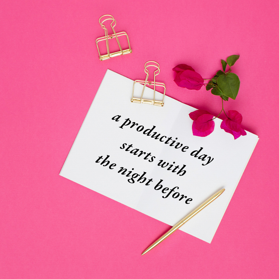 White notecard with the words "a productive day starts with the night before" typed out on it laying on a hot pink background surrounded by a gold pen and gold binder clips.